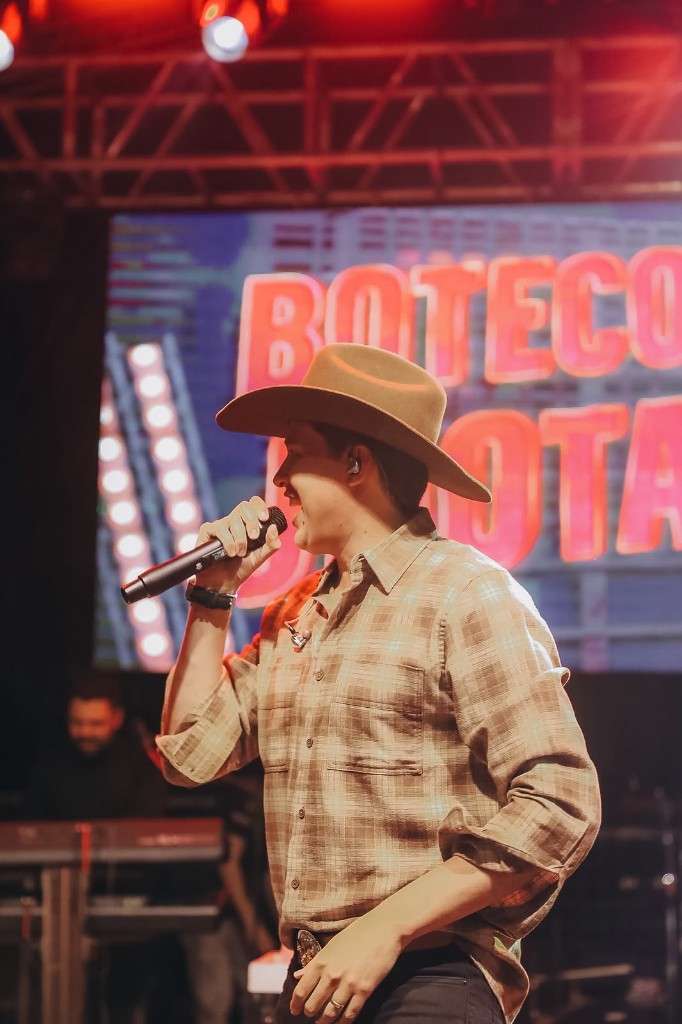 Jhotapê cantando ao vivo com chapéu no palco